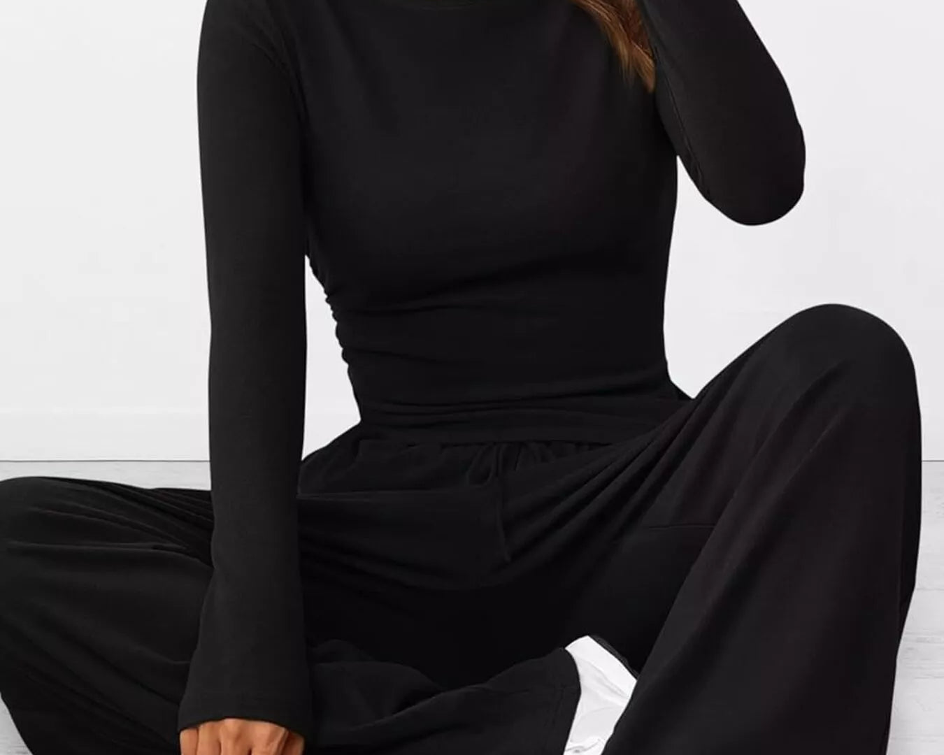 Person wearing a black long-sleeve jumpsuit sitting on a white floor.