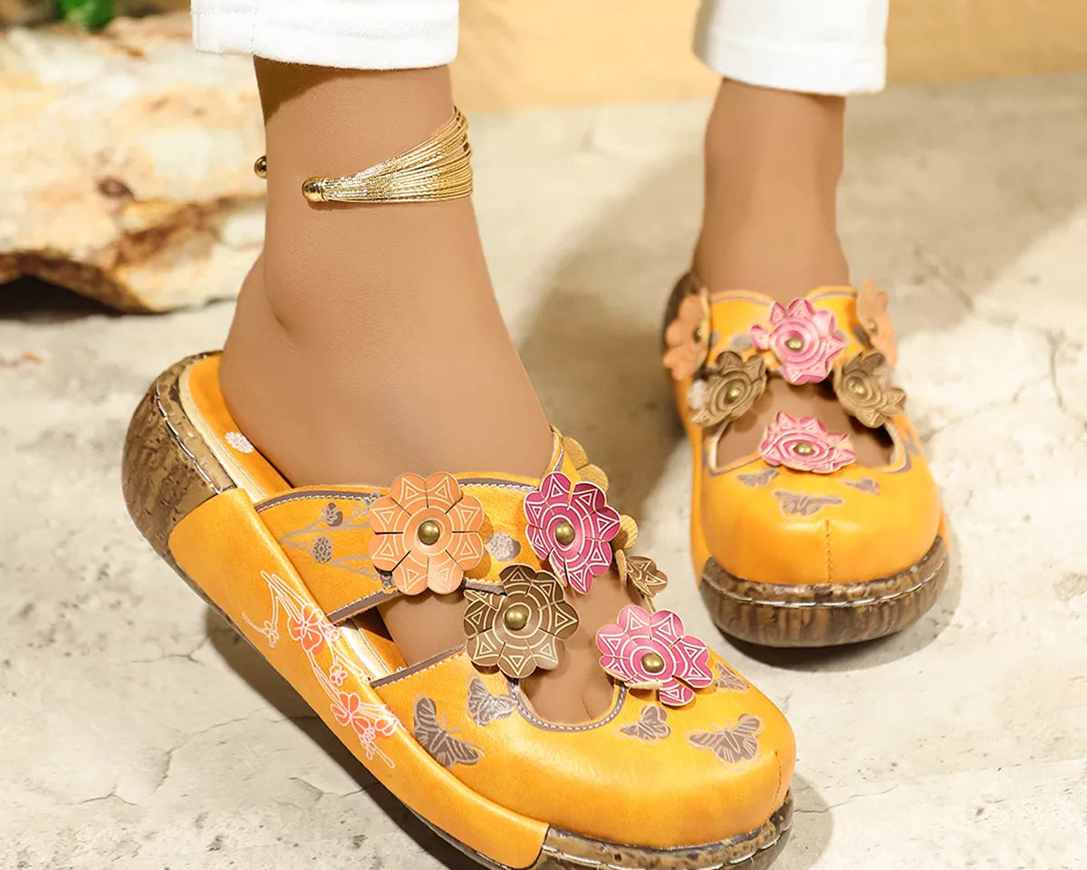 NEWYORKLISTED SHOE COLLECTION: Yellow sandals with floral designs worn by a person on a textured surface.