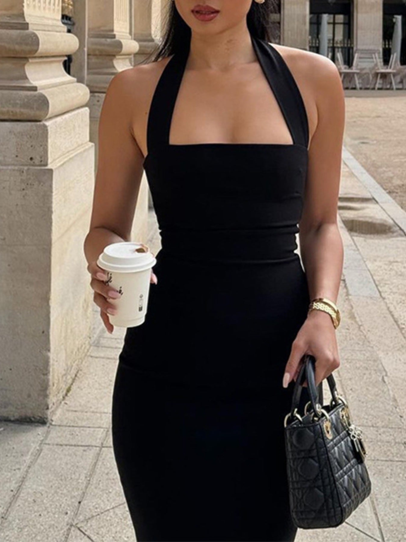 NEWYORKLISTED STYLE COLLECTION: Woman in a black dress holding a coffee cup and a handbag on a city street.