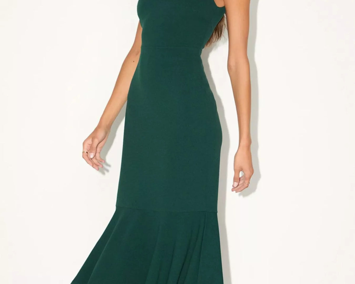 NEWYORKLISTED STYLE COLLECTION: A woman modeling a dark green midi dress with a square neckline, wide shoulder straps, and a flared ruffled hem, photographed against a plain off-white studio background.