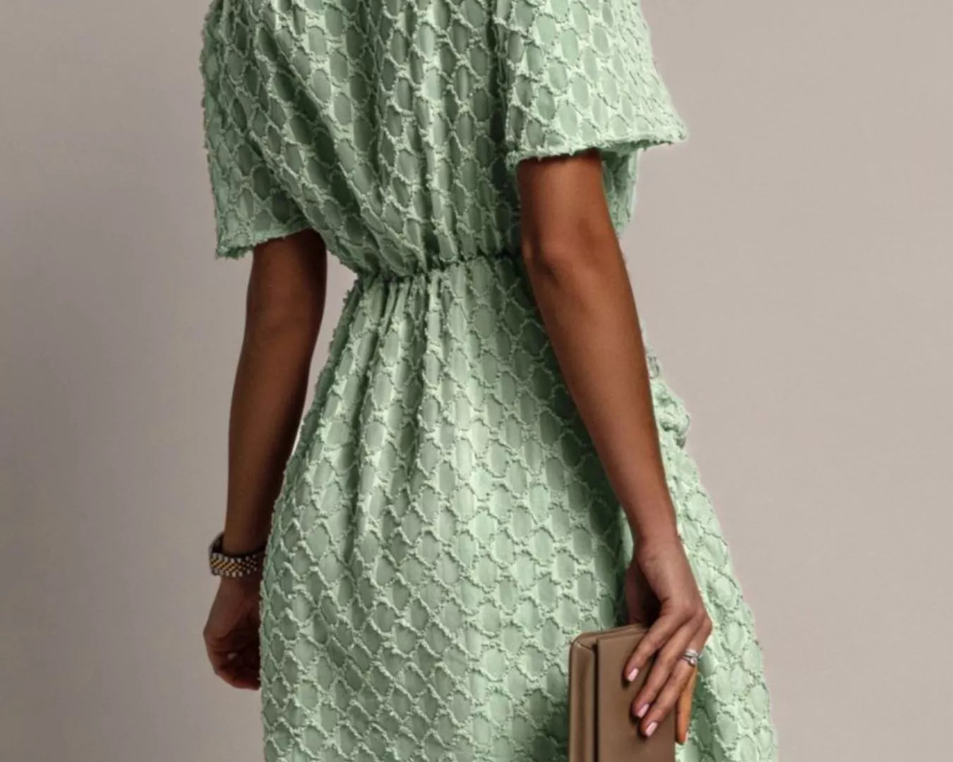 NEWYORKLISTED STYLE COLLECTION: Woman wearing a green patterned dress holding a beige clutch against a neutral background