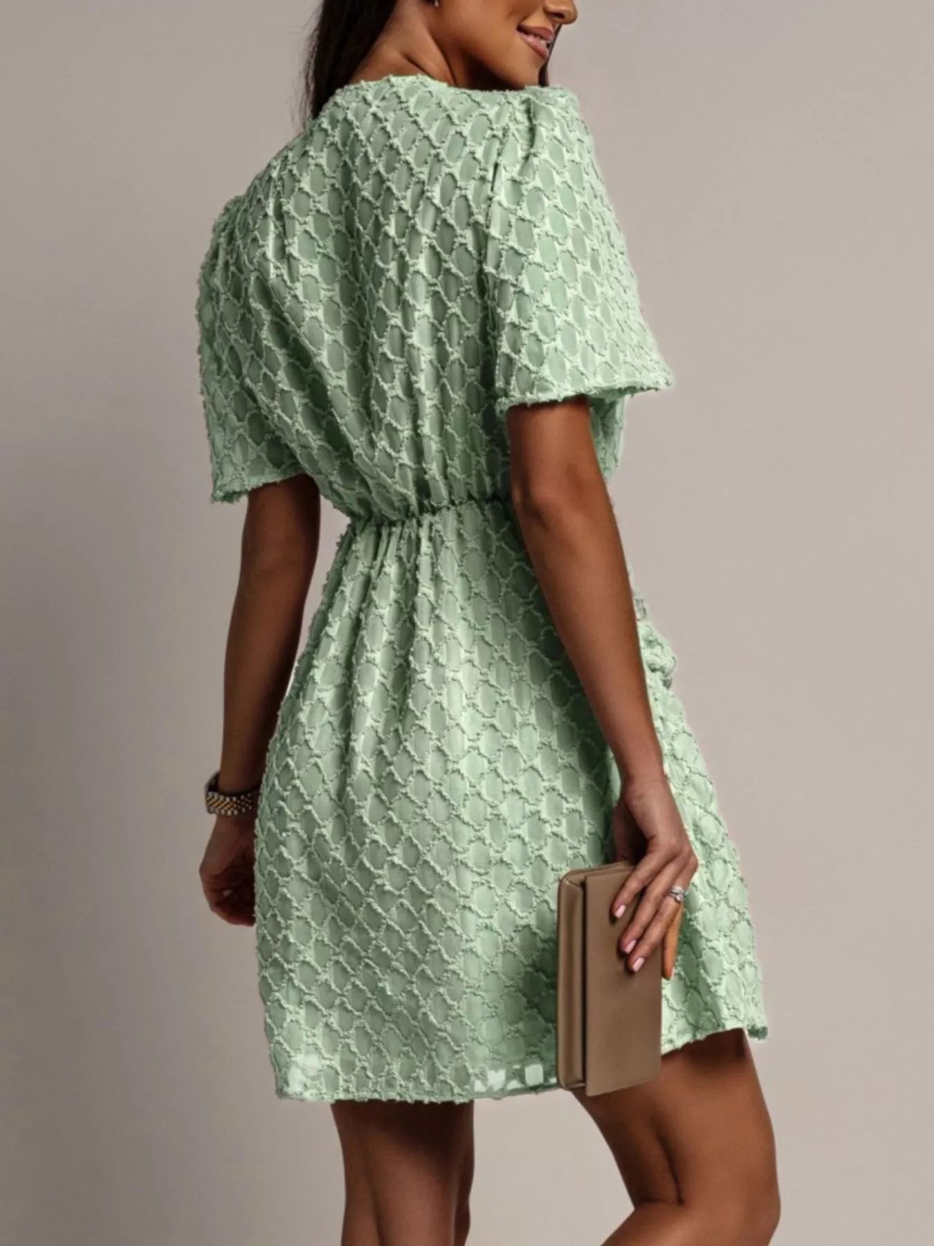 NEWYORKLISTED STYLE COLLECTION: Woman wearing a green patterned dress holding a beige clutch against a neutral background