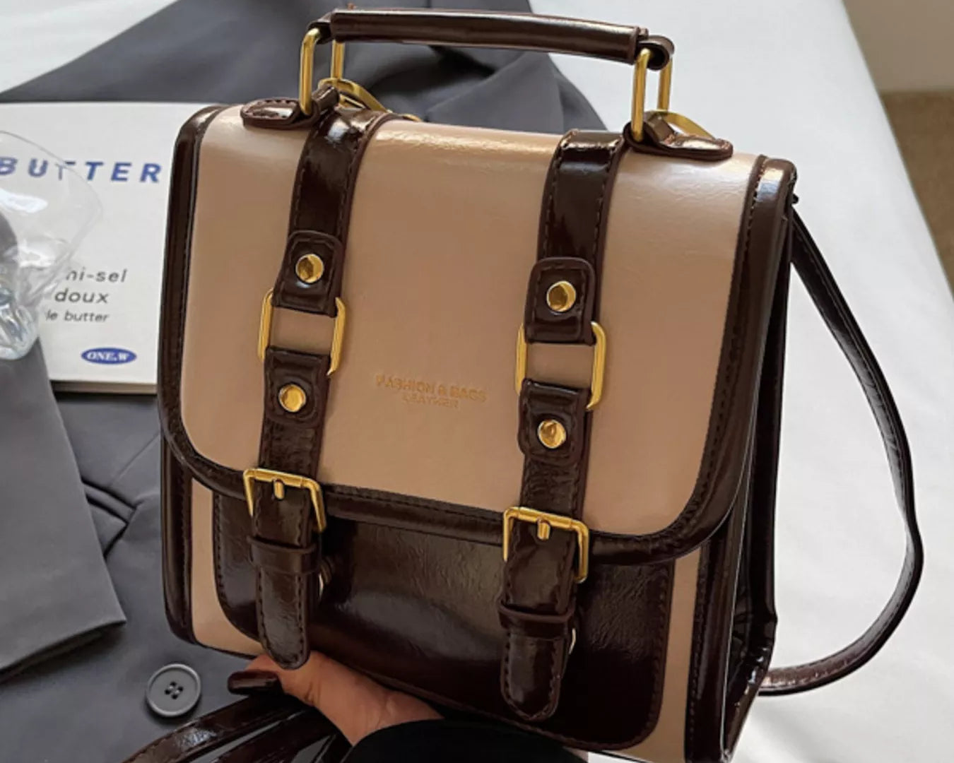 NEWYORKLISTED STYLE COLLECTION: Two-tone handbag with brown and beige colors held by a person, with a magazine in the background.