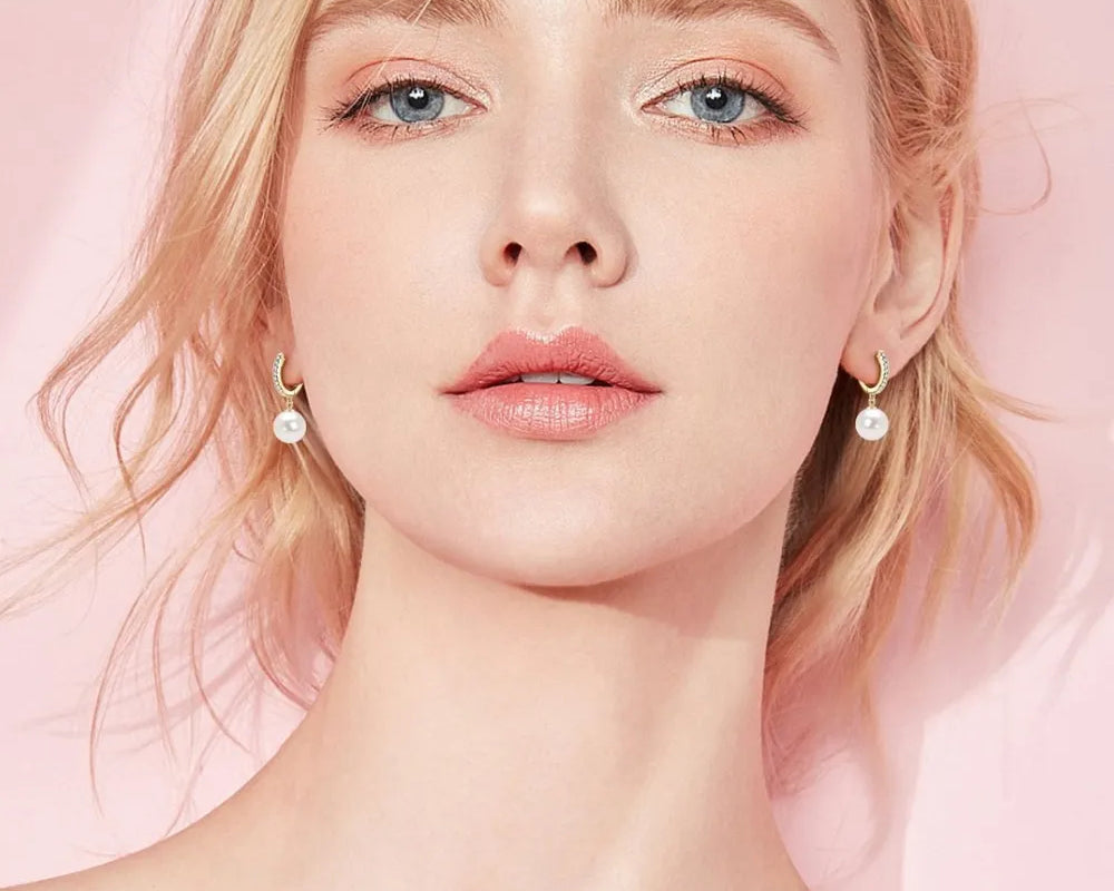 NYLD GLAMOUR COLLECTION by NEWYORKLISTED: Woman with pearl earrings against a pink background