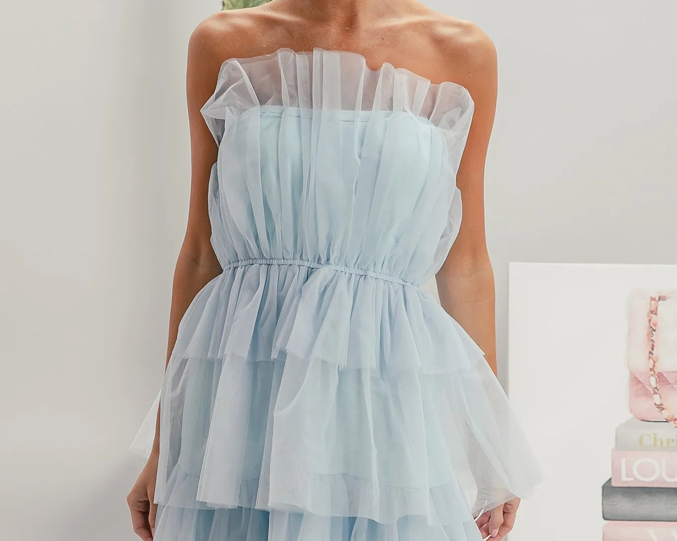 NEWYORKLISTED STYLE COLLECTION: Sleeveless Layered Organza Dress: Woman wearing a light blue strapless dress in a minimalistic setting with a 'Dior' magazine.