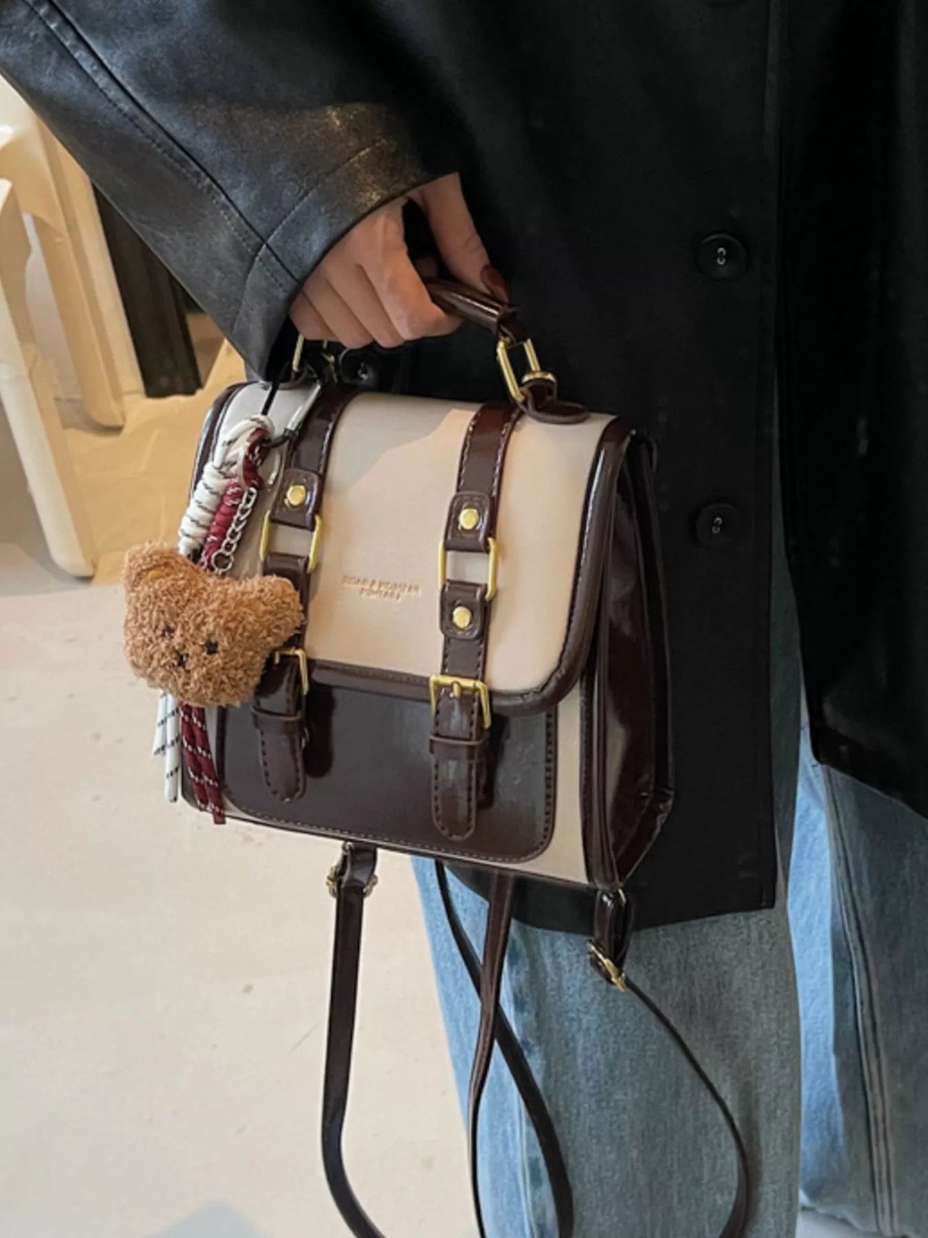 NEWYORKLISTED STYLE COLLECTION: Person holding a black and beige handbag with a teddy bear charm.