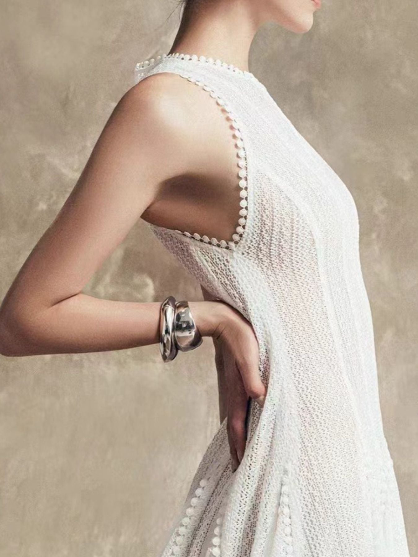 NEWYORKLISTED STYLE COLLECTION: Woman wearing a white dress with a textured back design, holding her arm with a bracelet.