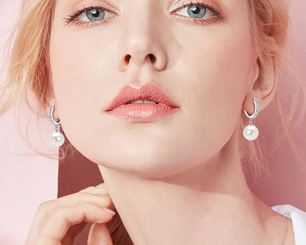 NYLD GLAMOUR COLLECTION by NEWYORKLISTED: Close-up of a person wearing pearl earrings against a pink background