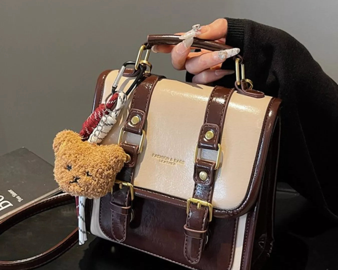 NEWYORKLISTED STYLE COLLECTION: Handbag with teddy bear charm held by a hand against a neutral background