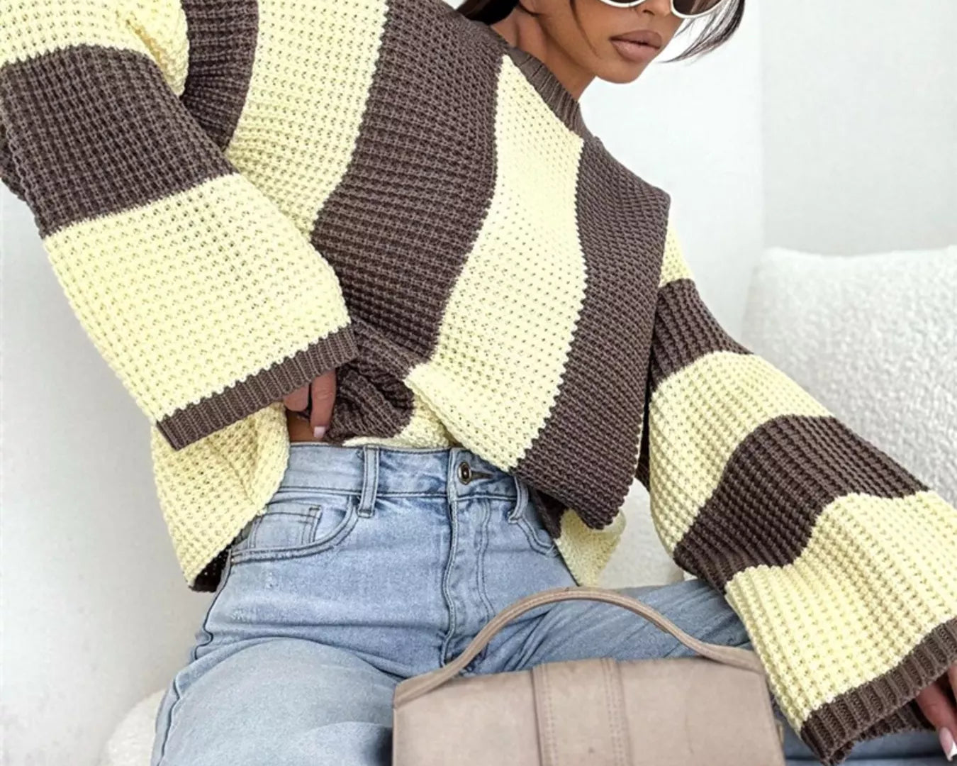 NEWYORKLISTED STYLE COLLECTION: Woman wearing a striped sweater and holding a handbag, sitting on a couch.