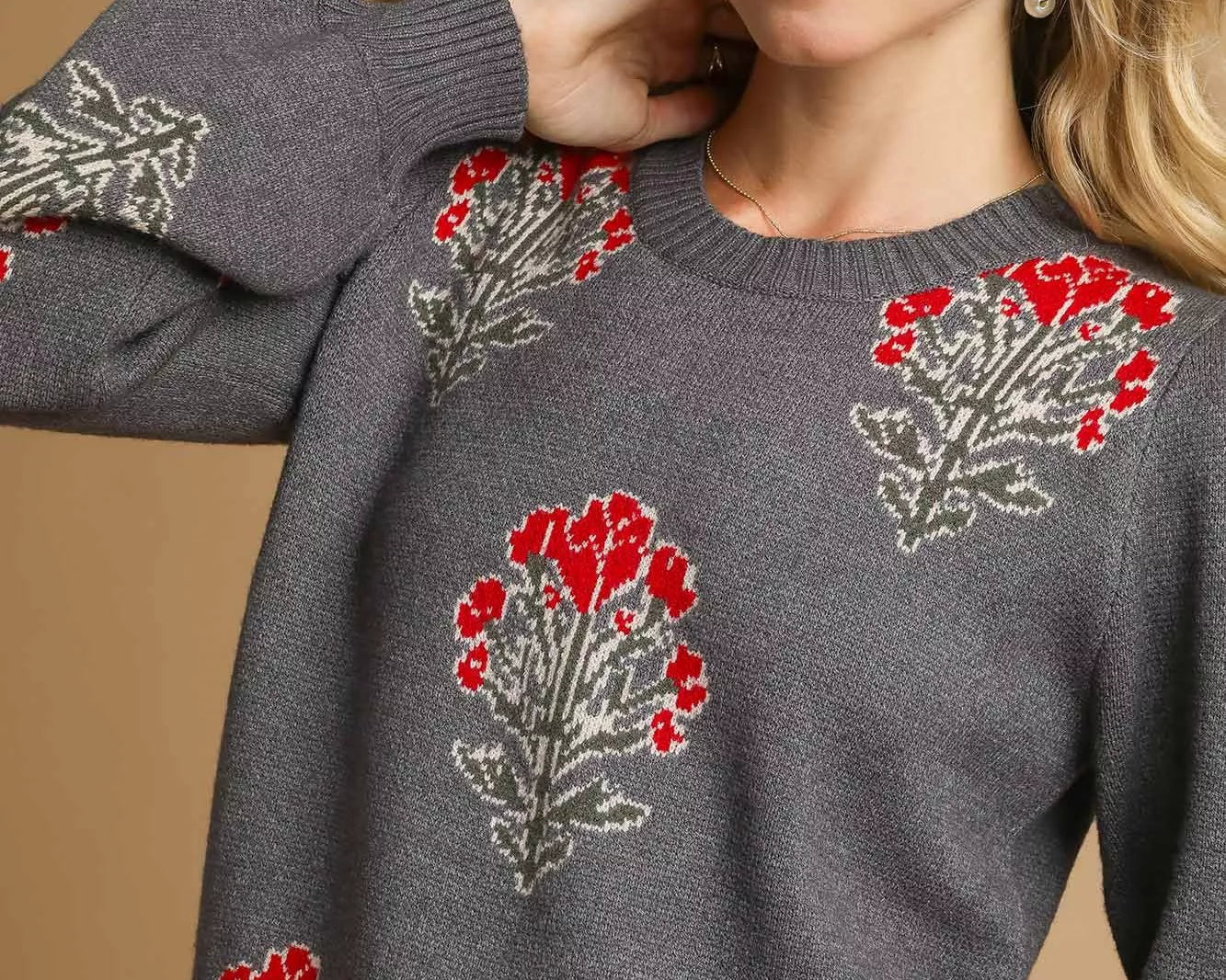NEWYORKLISTED STYLE COLLECTION: Woman wearing a gray sweater with red floral patterns on a beige background