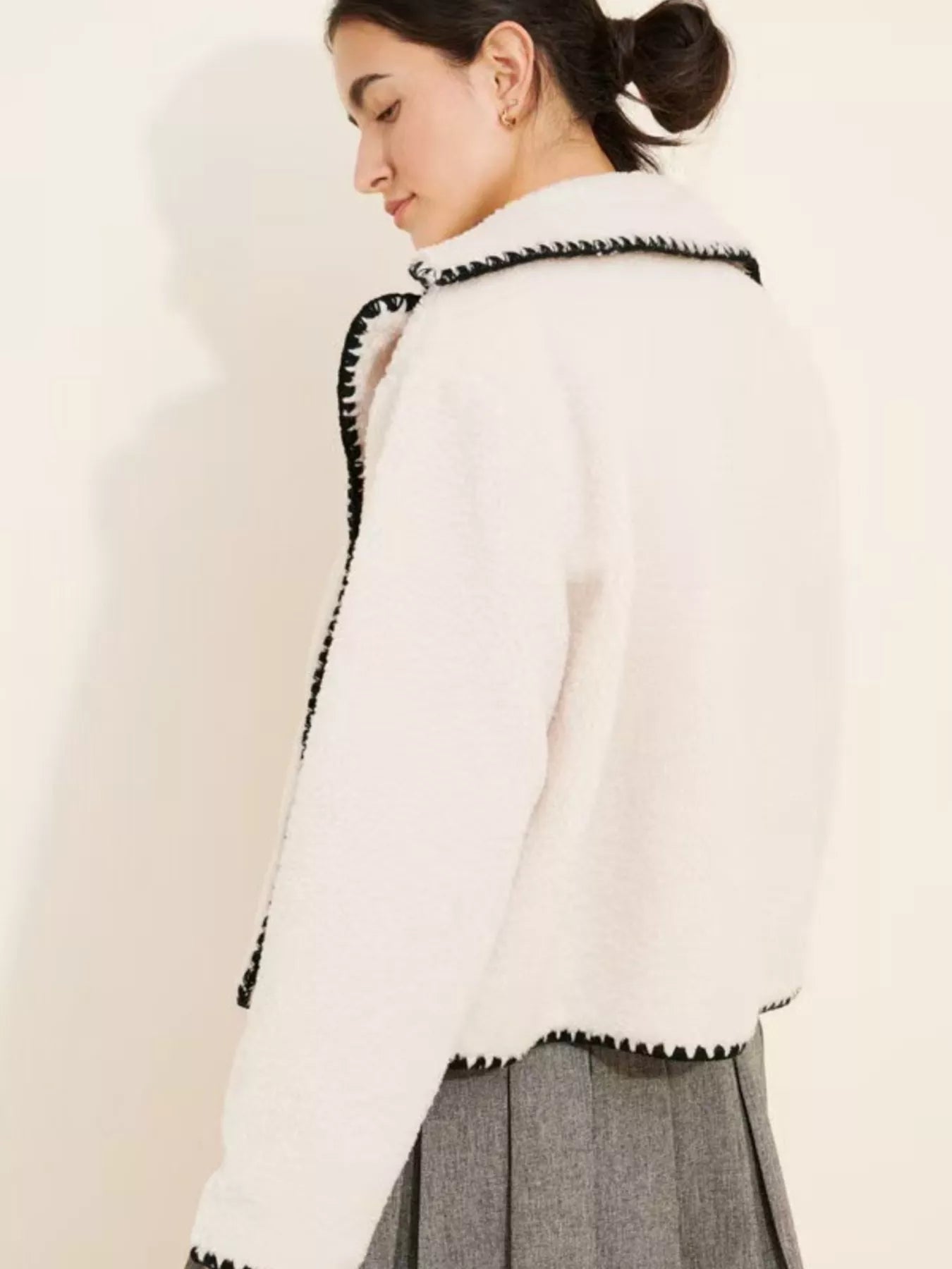 NEWYORKLISTED STYLE COLLECTION: Woman wearing a white sweater with black trim on a plain background