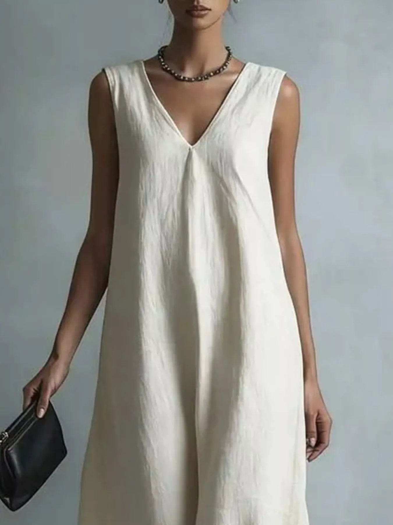 NEWYORKLISTED STYLE COLLECTION: A woman wearing a sleeveless, V-neck cream linen jumpsuit, holding a black leather clutch against a neutral gray background.