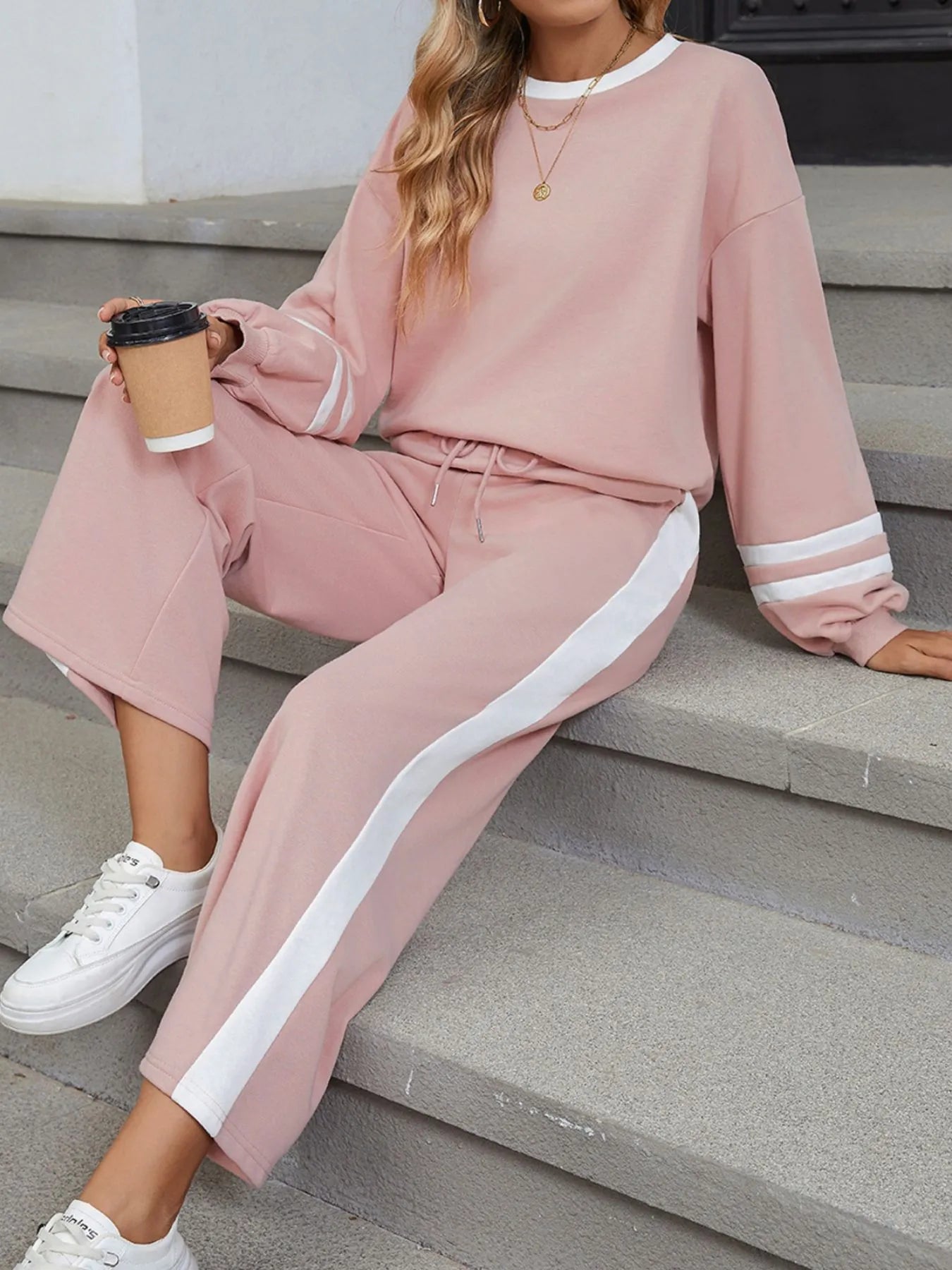 NEWYORKLISTED Comfort Collection: Person wearing a pink tracksuit with white stripes sitting on steps.