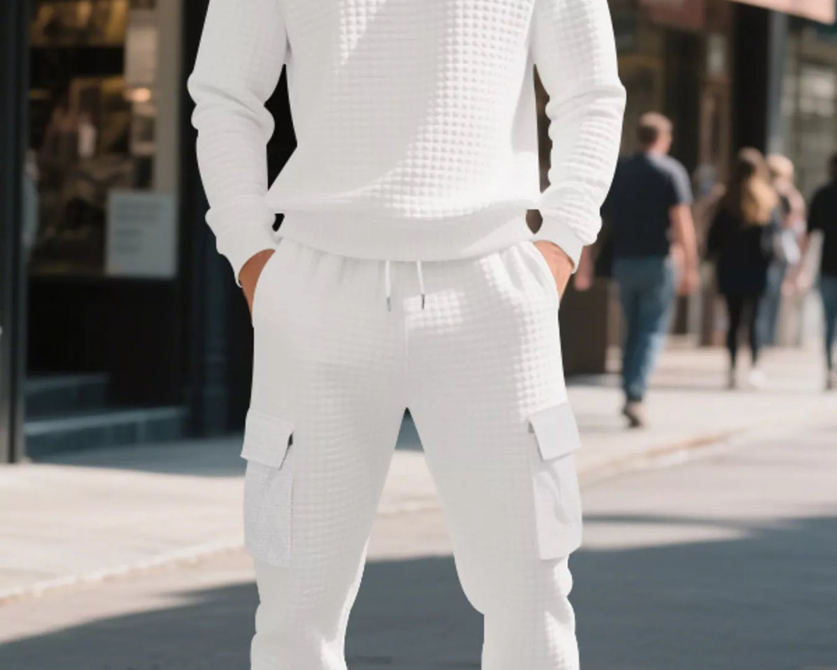 NEWYORKLISTED ATLAS MEN'S COLLECTION: A man wearing a matching white textured long-sleeve sweatshirt and cargo jogger pants stands on a city sidewalk, with blurred pedestrians and storefronts in the background.