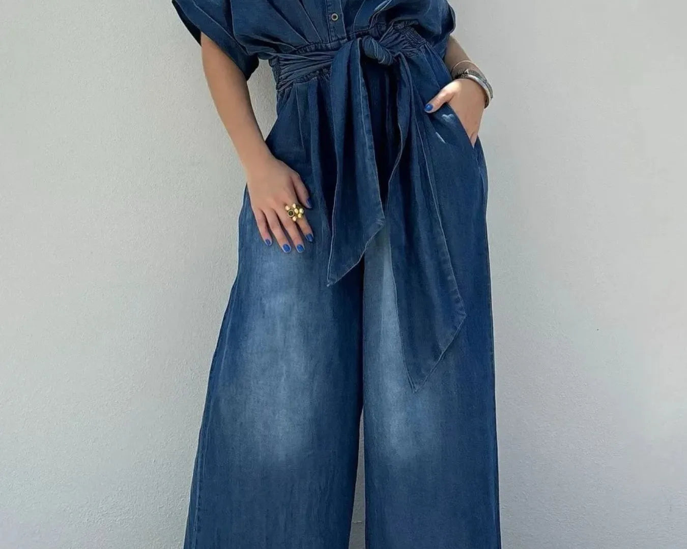 NEWYORKLISTED STYLE COLLECTION: Person wearing a blue denim jumpsuit against a plain background