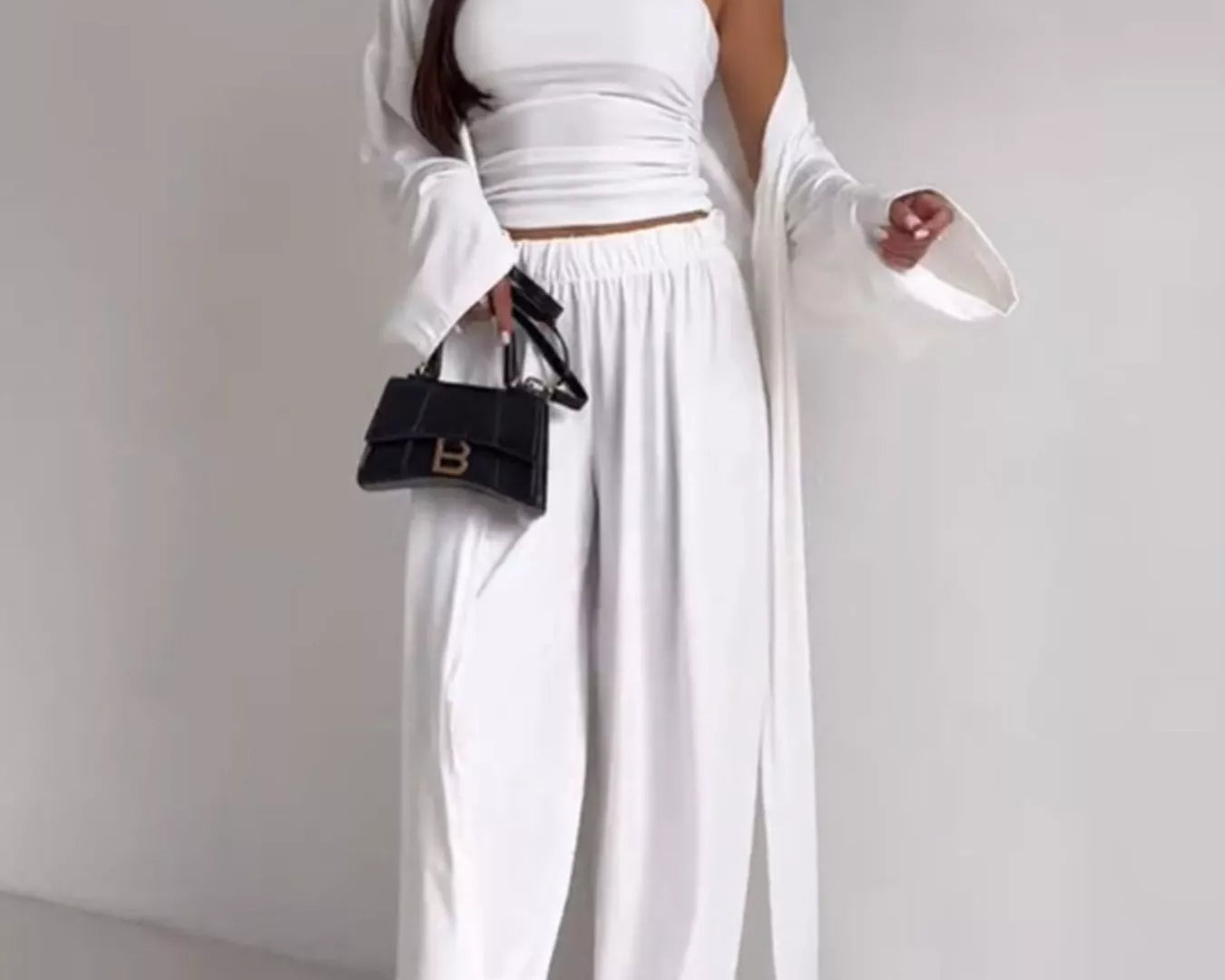 NEWYORKLISTED COMFORT COLLECTION: Woman wearing a white outfit with a black handbag on a plain background