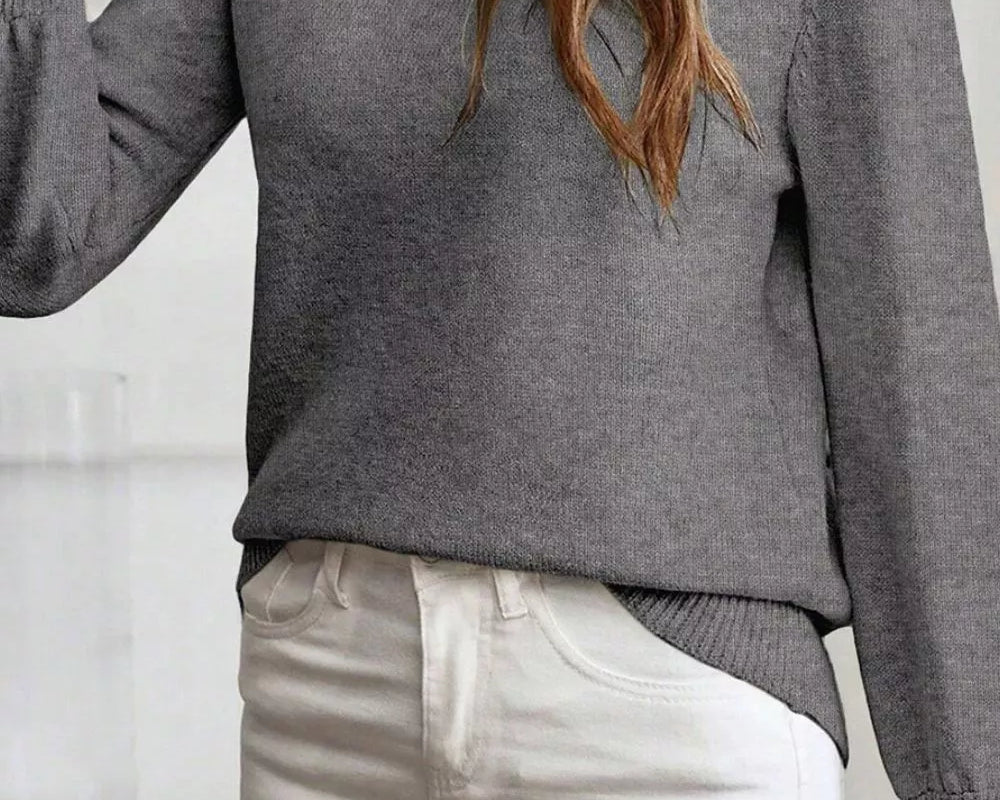 NEWYORKLISTED STYLE COLLECTION: Person wearing a gray sweater and light-colored pants indoors.