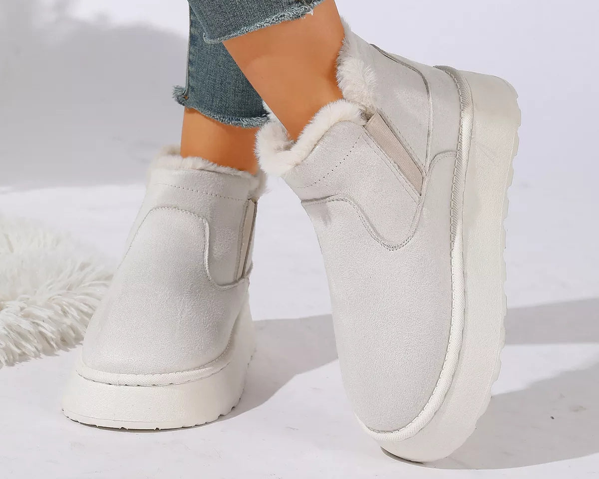 NEWYORKLISTED SHOE COLLECTION: A pair of off-white platform slip-on boots with fluffy white faux-fur trim, shown on a model wearing blue jeans against a white studio background.