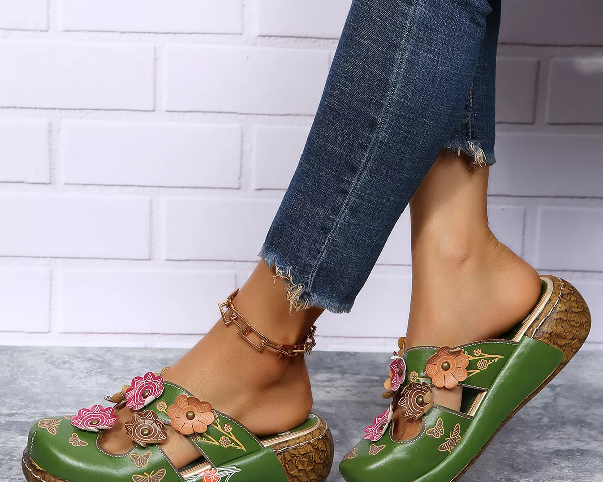 NEWYORKLISTED SHOE COLLECTION: Green sandals with floral designs worn by a person against a white brick wall.