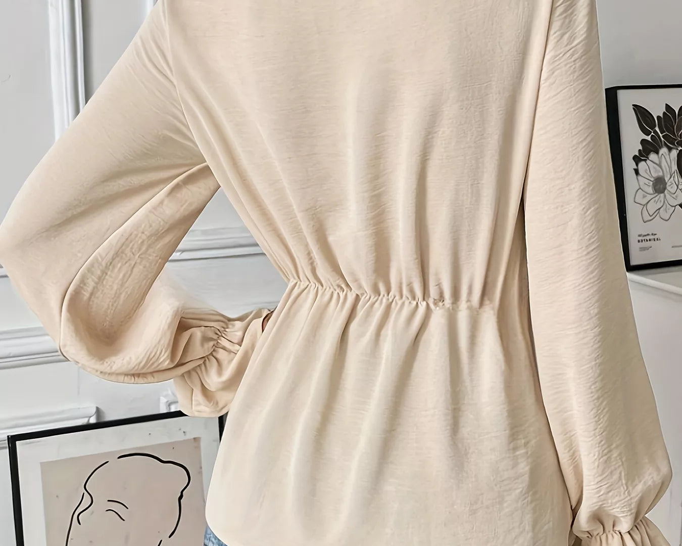 NEWYORKLISTED STYLE COLLECTION: Woman wearing a beige long-sleeve top with a subtle waistband, standing indoors.