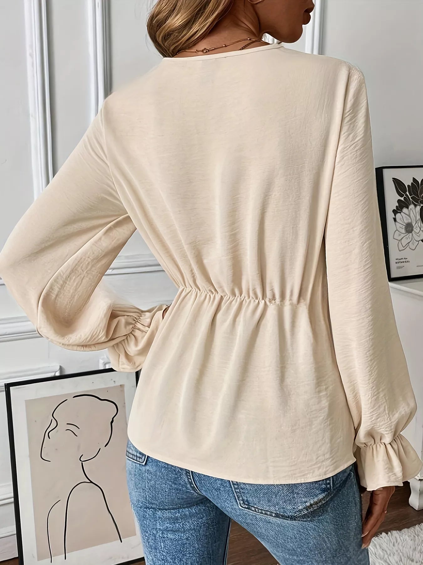 NEWYORKLISTED STYLE COLLECTION: Woman wearing a beige long-sleeve top with a subtle waistband, standing indoors.