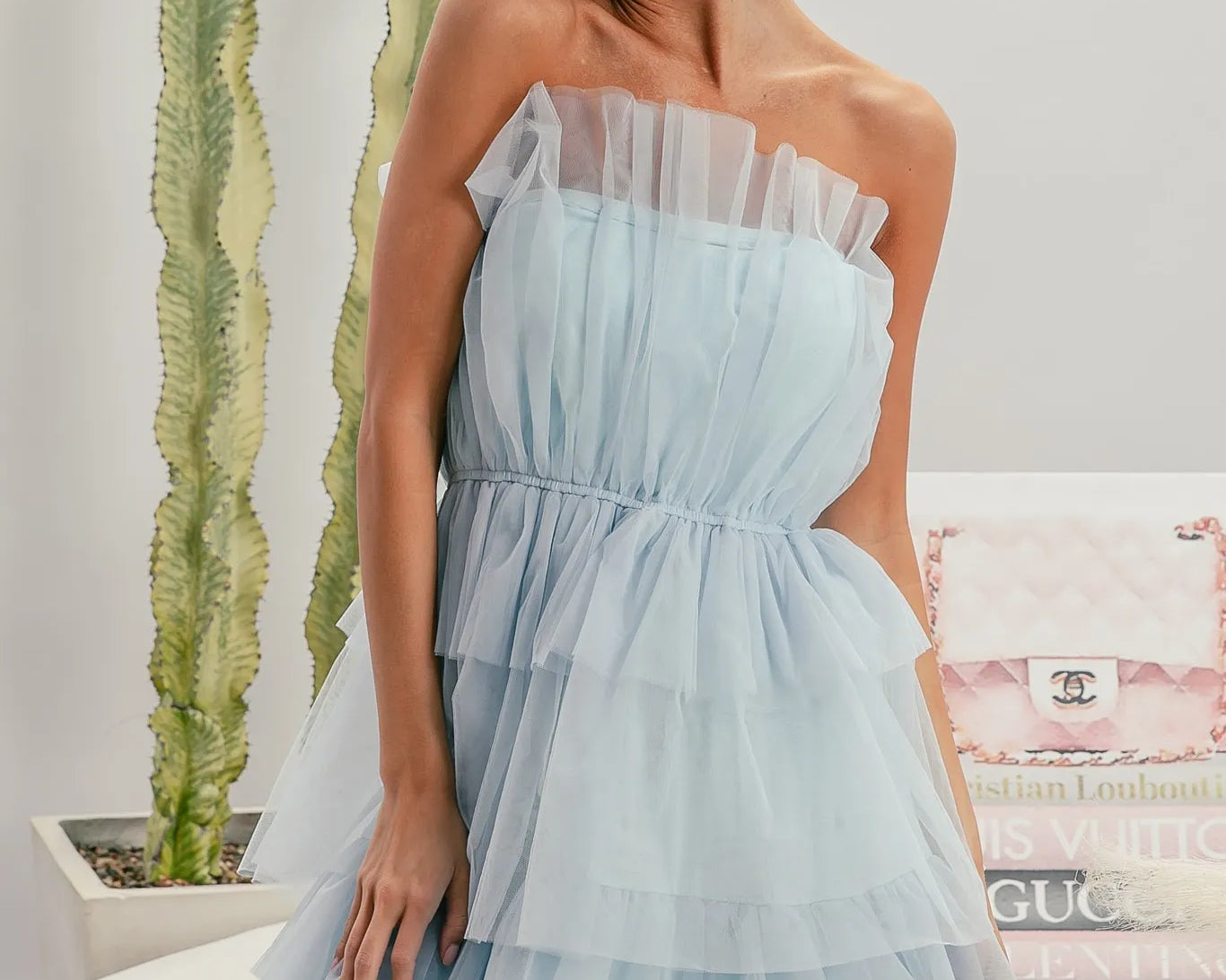 NEWYORKLISTED STYLE COLLECTION: Sleeveless Layered Organza Dress: Woman wearing a light blue strapless dress with a blurred indoor background