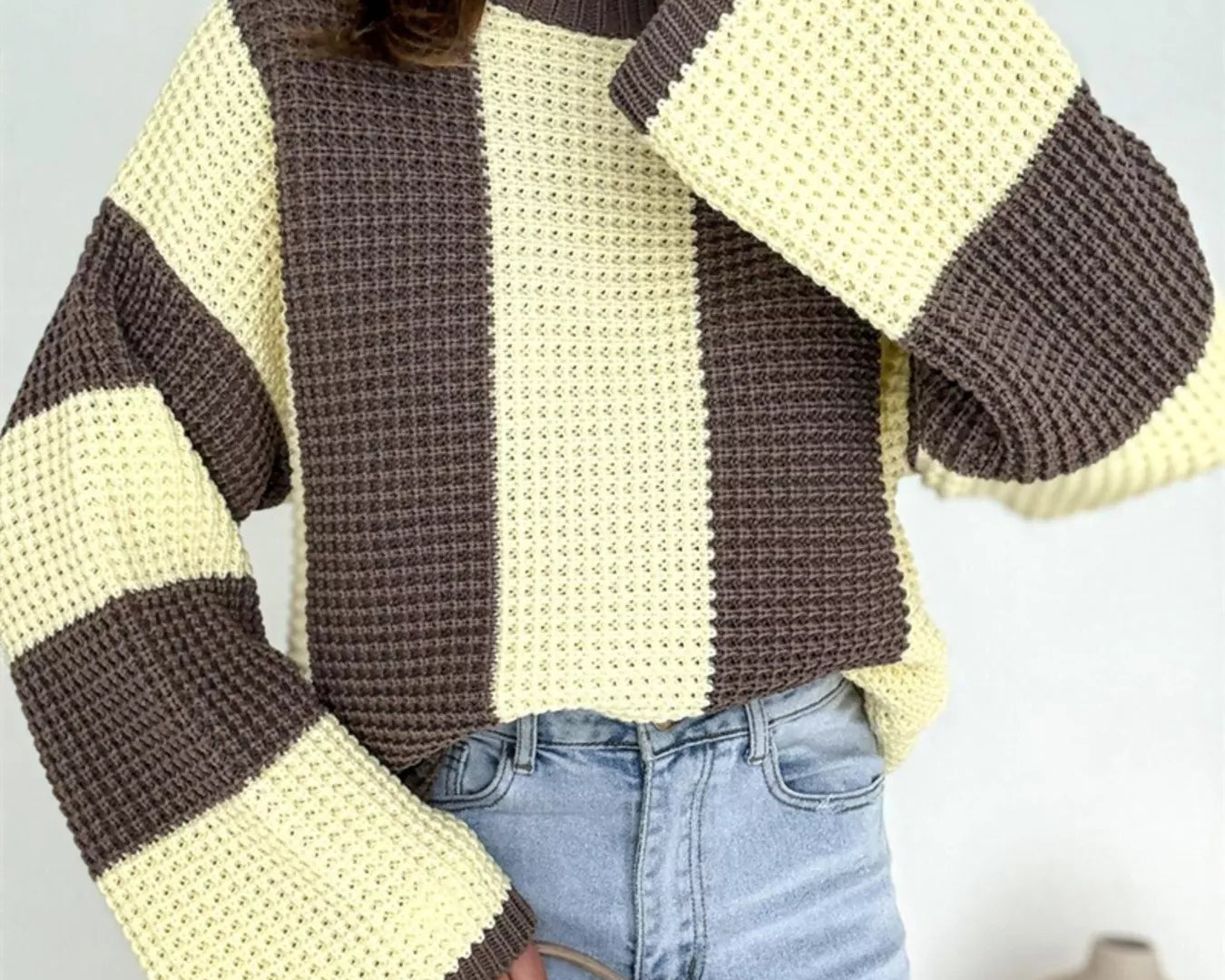 NEWYORKLISTED STYLE COLLECTION: Person wearing a striped sweater with brown and yellow colors, standing against a light gray background.