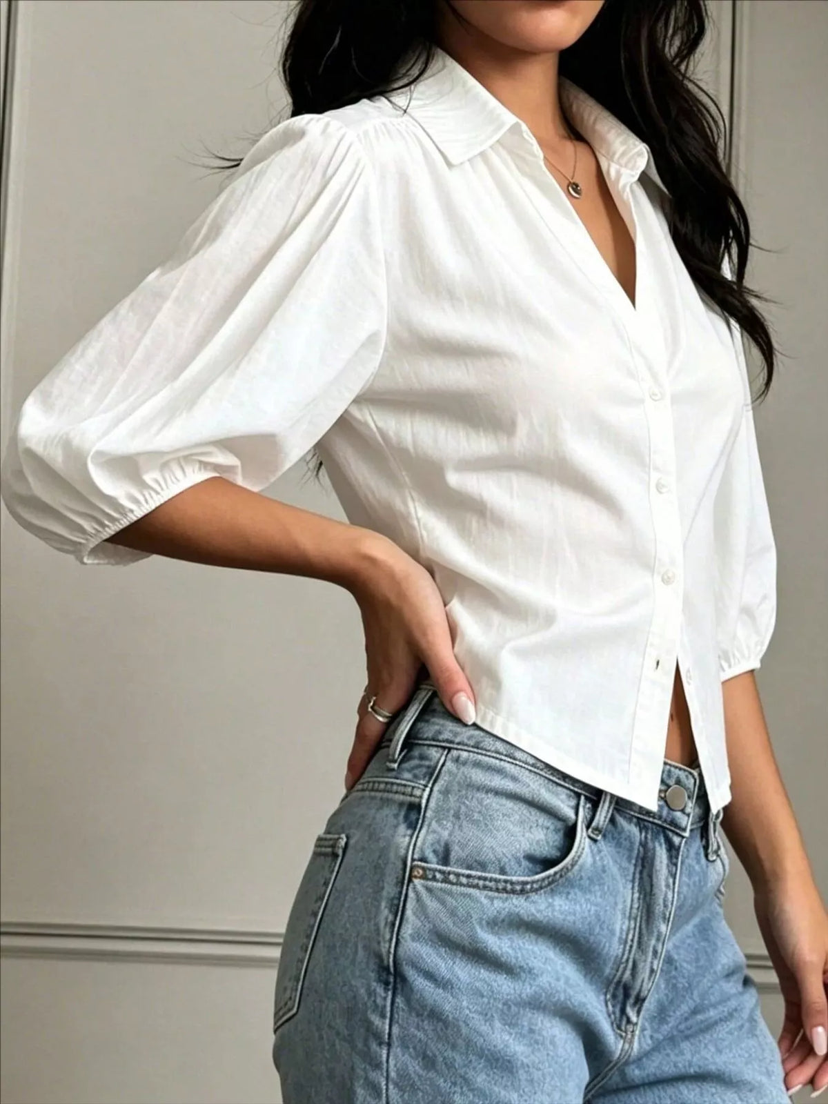 NEWYORKLISTED STYLE COLLECTION: A woman wearing a white short puff-sleeve button-up shirt tucked into light-wash blue jeans, shown from the neck down against a neutral indoor wall.