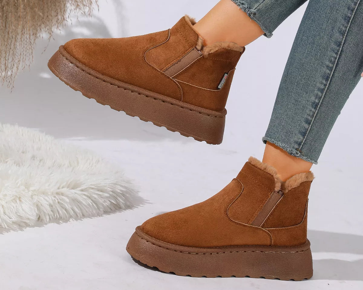 NEWYORKLISTED SHOE COLLECTION: A pair of women's brown suede ankle boots with a plush faux-fur lining and chunky platform soles, shown on a model wearing blue jeans against a white studio background with decorative faux fur.