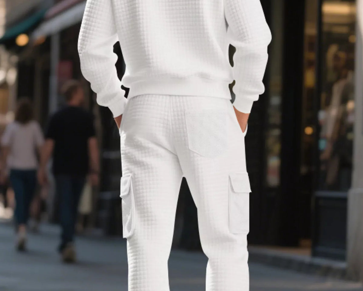 NEWYORKLISTED ATLAS MEN'S COLLECTION: A man standing on a city street, viewed from the back, wearing a matching white waffle-knit crewneck sweatshirt and cargo pants set.