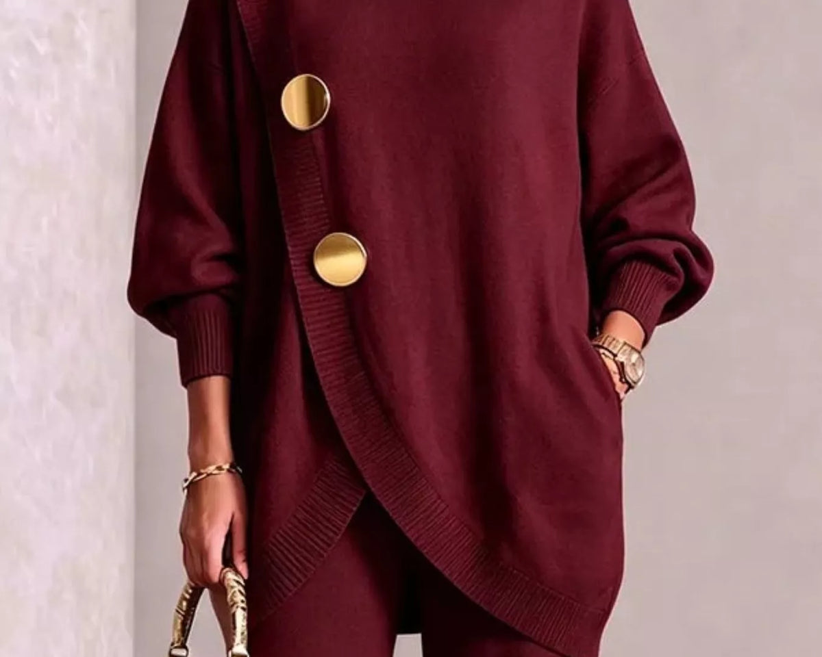 NEWYORKLISTED STYLE COLLECTION: A woman models a deep burgundy knit turtleneck sweater with oversized gold buttons and matching trousers, holding a small gold handbag against a neutral textured wall.