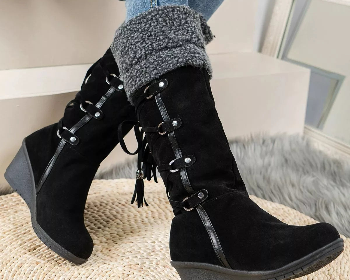 NEWYORKLISTED SHOE COLLECTION: Black lace-up boots worn with blue jeans and gray sweater cuffs, sitting on a textured surface.