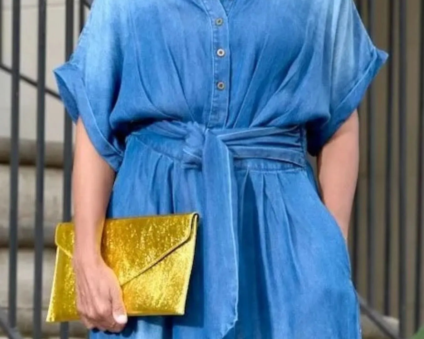 NEWYORKLISTED STYLE COLLECTION: Person wearing a blue dress holding a gold clutch against a neutral background
