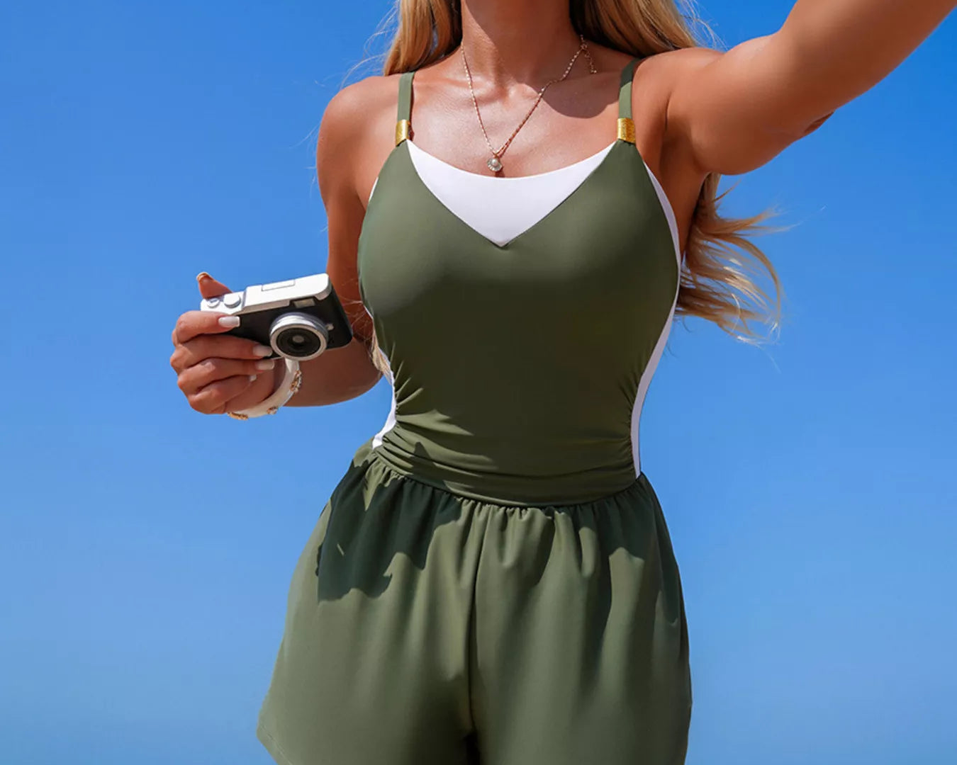NEWYORKLISTED EDEN COLLECTION: Woman in a green romper taking a selfie on a beach with clear blue sky and ocean.