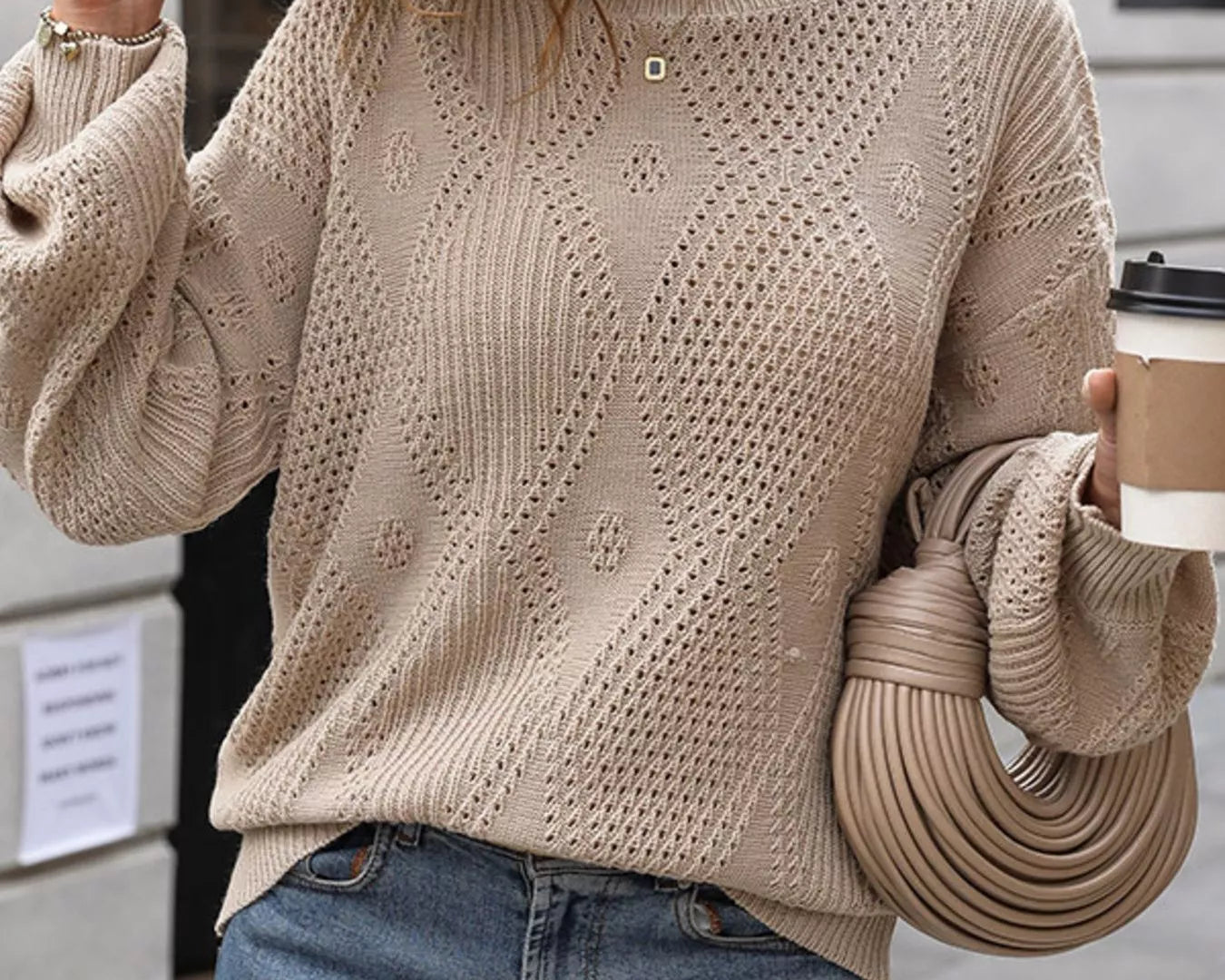 NEWYORKLISTED STYLE COLLECTION: Woman wearing a beige knit sweater and blue jeans, holding a beige handbag and a coffee cup.