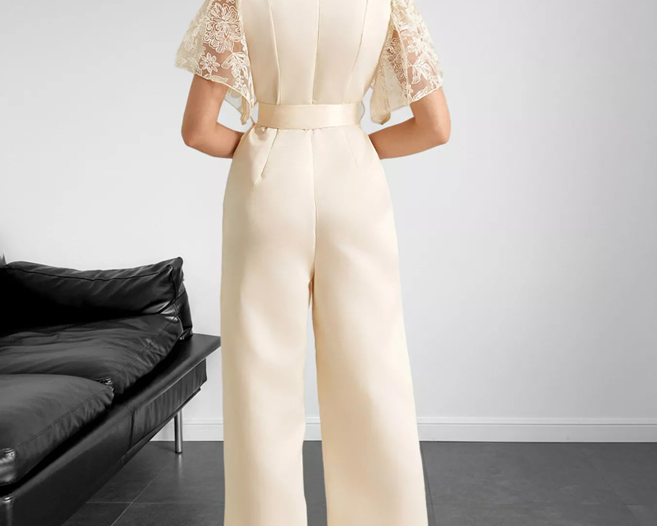 NEWYORKLISTED STYLE COLLECTION: Woman wearing a beige jumpsuit with lace sleeves in a minimalistic room.