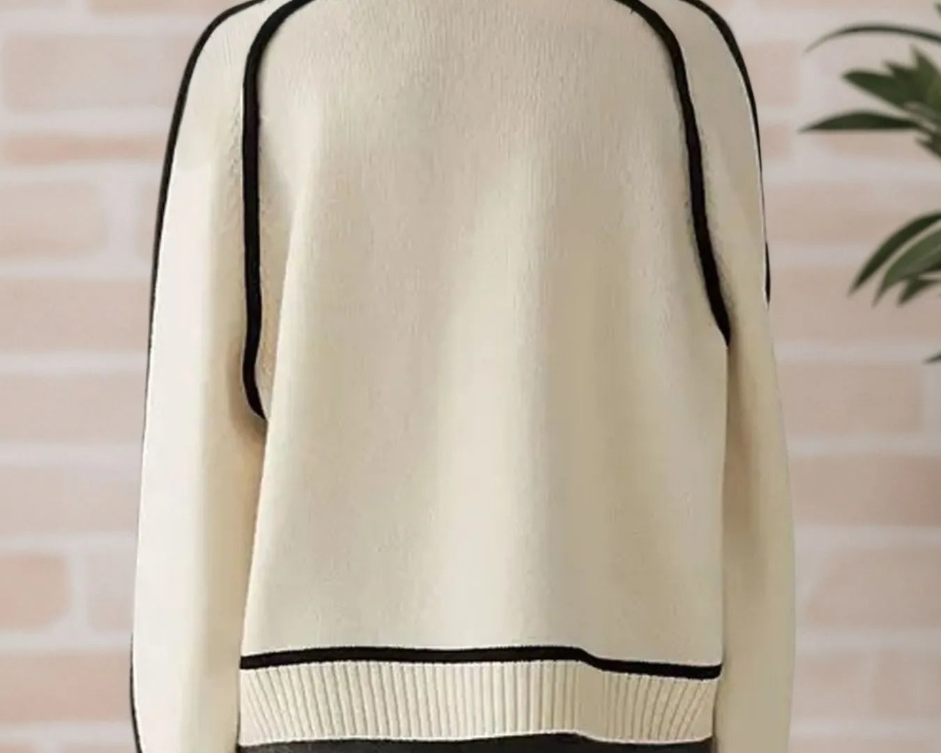 NEWYORKLISTED STYLE COLLECTION: Beige sweater with black trim worn by a person against a brick wall.