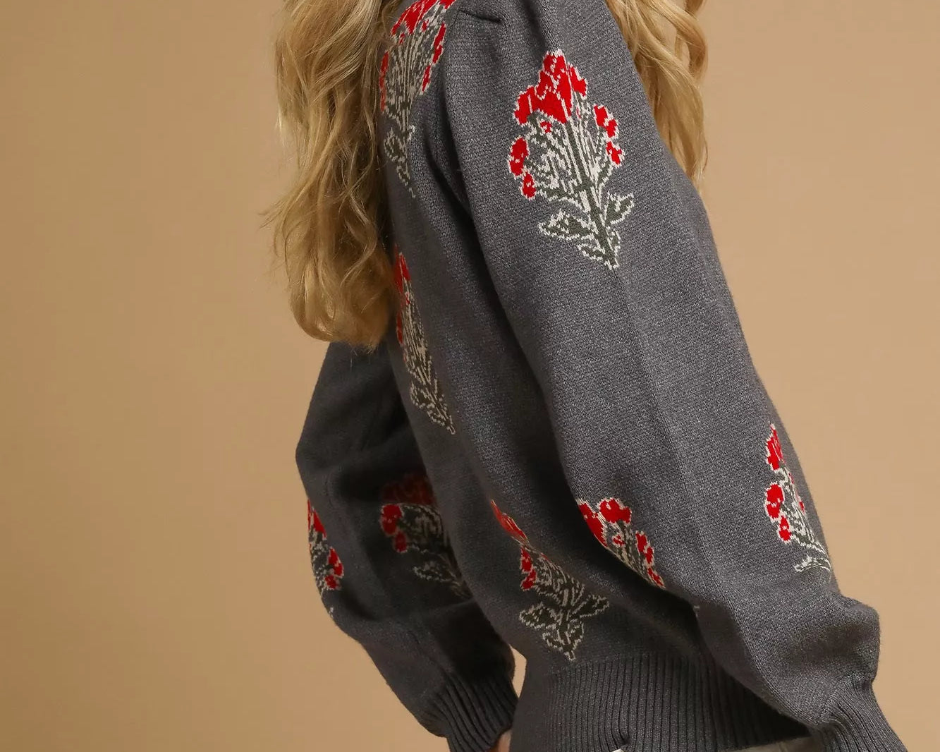 NEWYORKLISTED STYLE COLLECTION: Woman wearing a charcoal gray sweater with red floral embroidery on a beige background