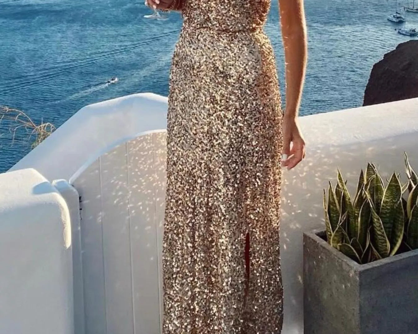 NEWYORKLISTED STYLE COLLECTION: Woman in a sparkly one-shoulder dress holding a glass of wine by the ocean.