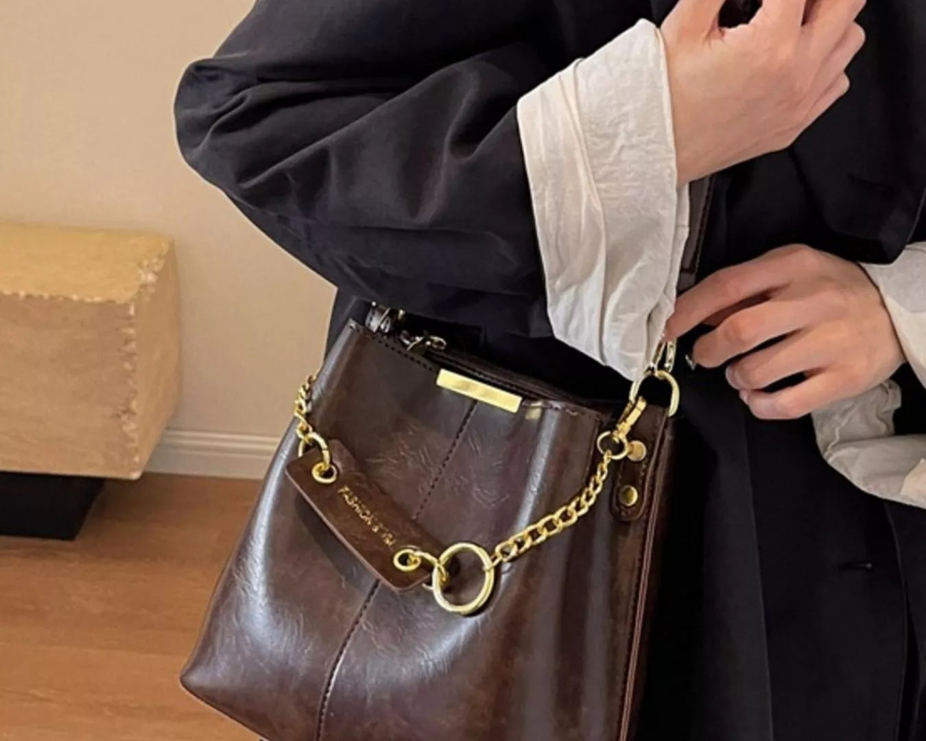 Person holding a brown leather handbag with gold chain detail indoors. New York Listed Style Collection