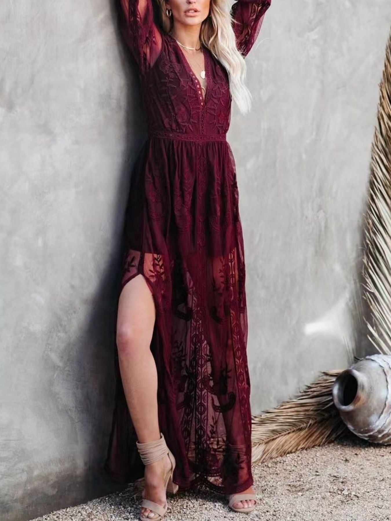 NEWYORKLISTED STYLE COLLECTION: Woman wearing a burgundy lace dress against a textured wall.