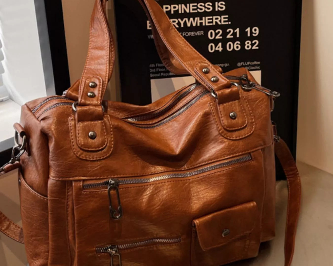 NEWYORKLISTED STYLE COLLECTION: Brown leather handbag on a reflective surface with a blurred background