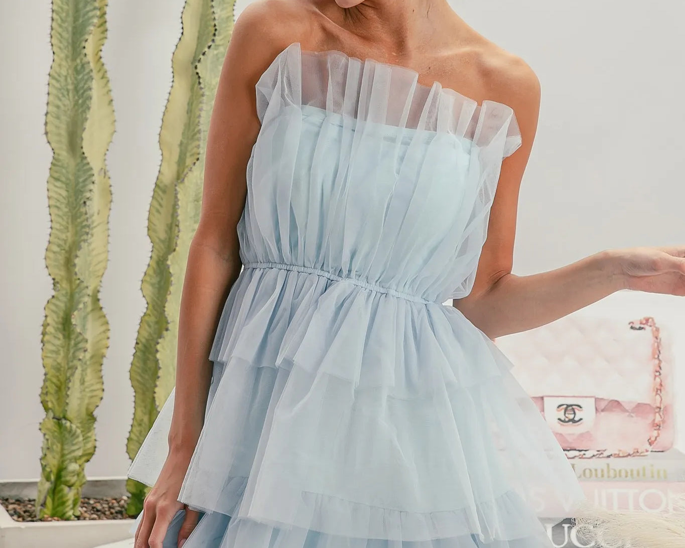 NEWYORKLISTED STYLE COLLECTION: Sleeveless Layered Organza Dress Woman wearing a light blue strapless dress with sunglasses, standing in front of a cactus plant.