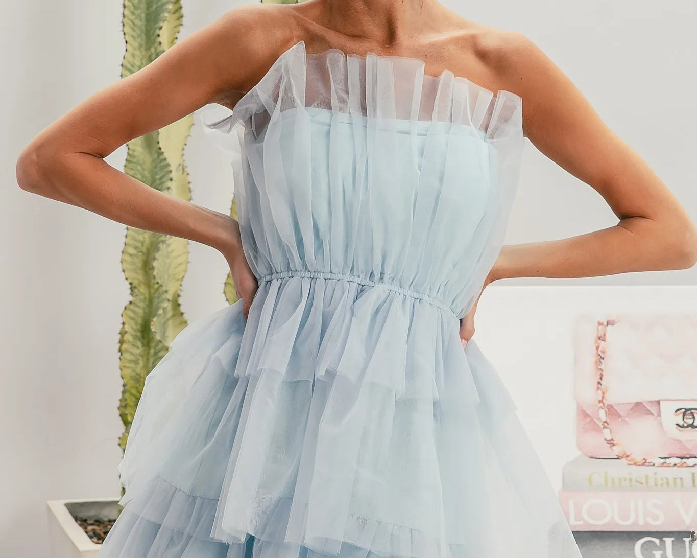 NEWYORKLISTED STYLE COLLECTION: Sleeveless Layered Organza Dress Woman wearing a light blue dress and sunglasses, standing in front of a stack of books with visible brand names.