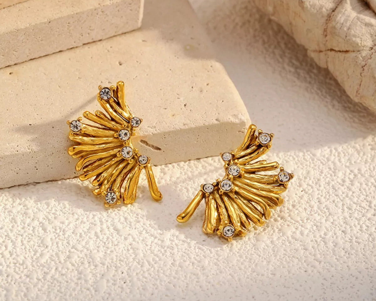 NYLD Glamour Collection by NEWYORKLISTED: Gold earrings with gemstones on a textured beige surface