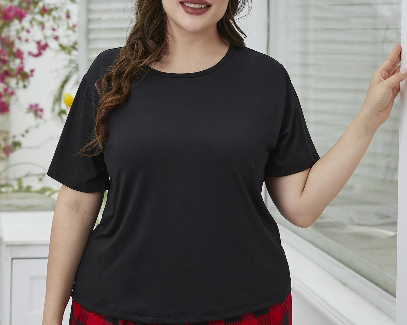 NEWYORKLISTED Intimate Apparel: Woman wearing a black top and red plaid shorts in a bright room.