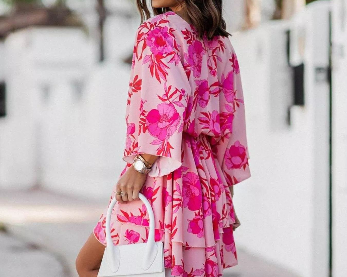 NEWYORKLISTED STYLE COLLECTION: Woman wearing a pink floral dress holding a white handbag on a street.
