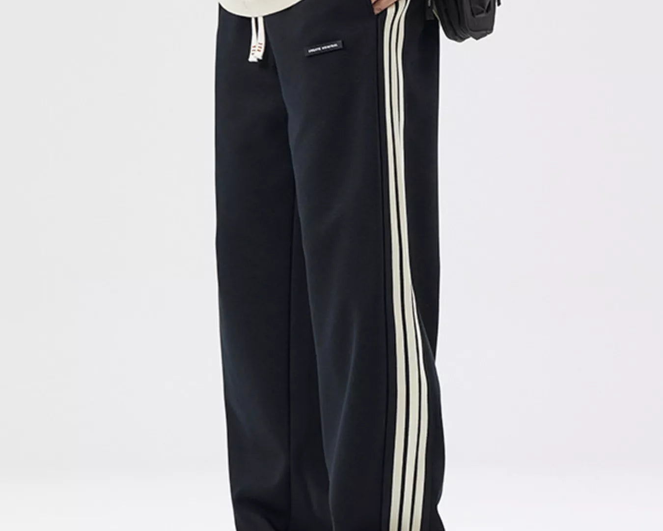 NEWYORKLISTED ATLAS MEN's COLLECTION: Black track pants with white stripes worn by a person on a white background