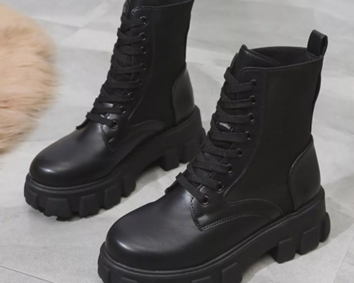 NEWYORKLISTED SHOE COLLECTION: Pair of black leather boots with thick soles on a light gray surface.